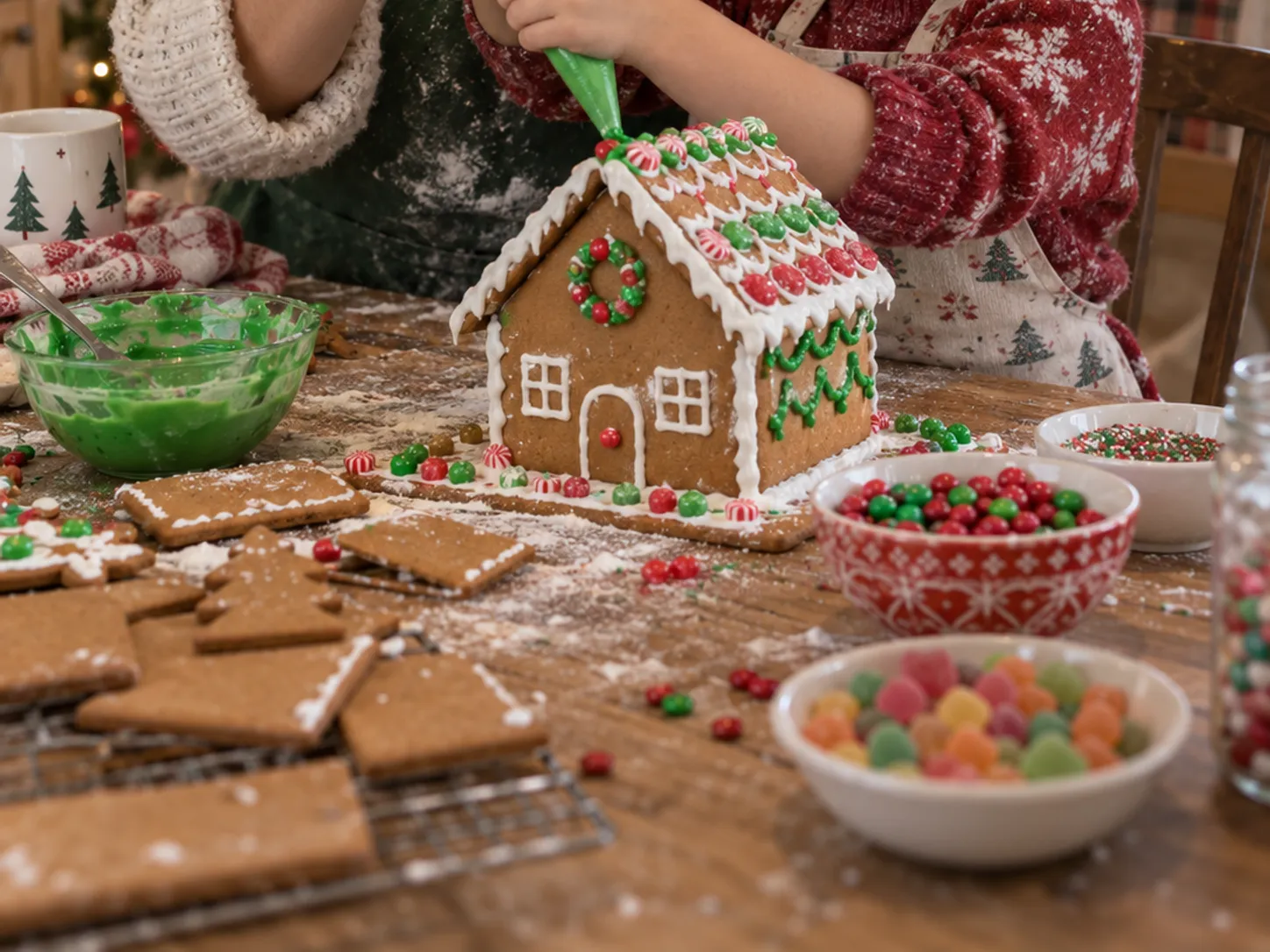 Parent and child decorating a gingerbread house at a messy kitchen table